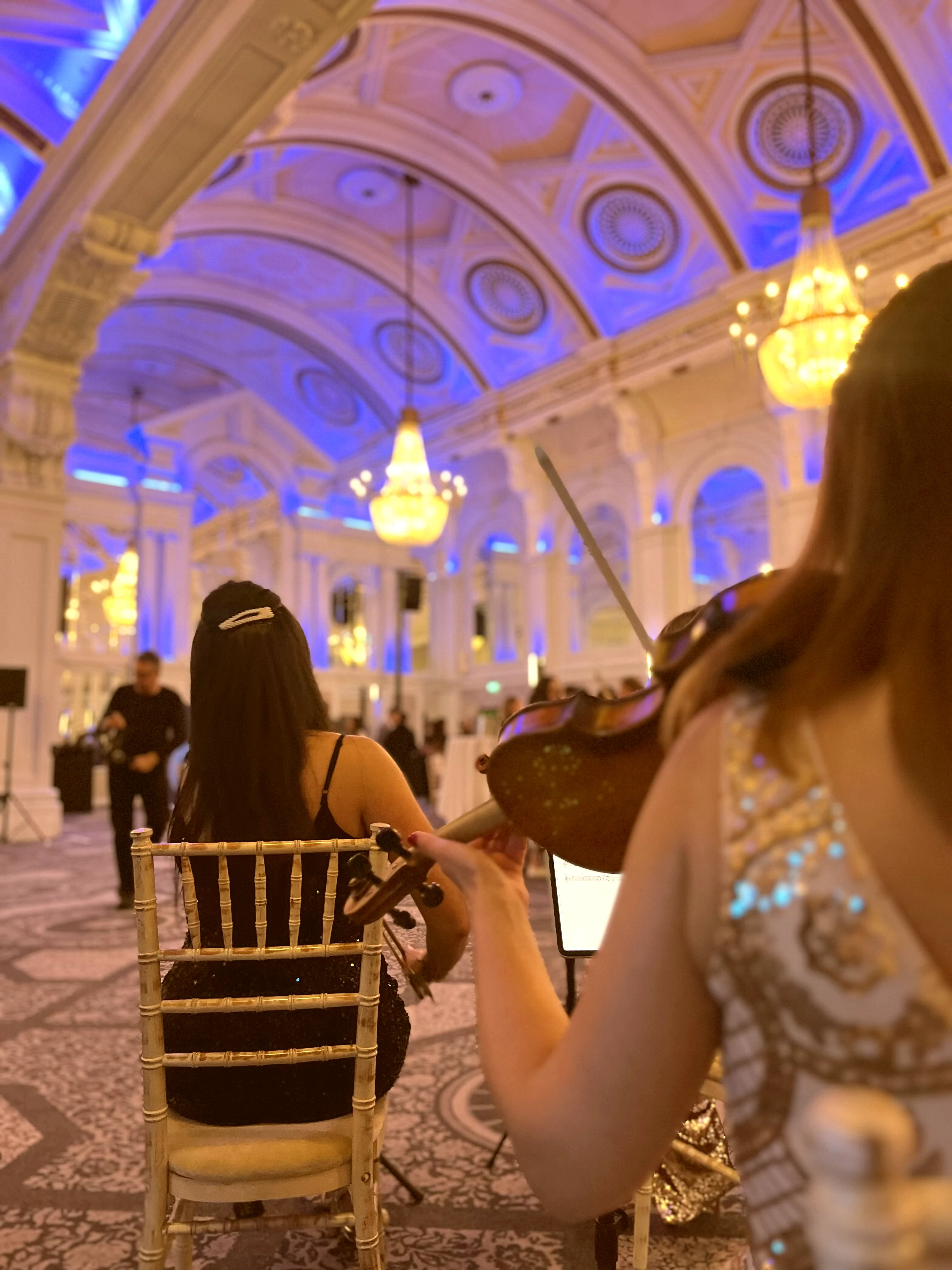 String players performing in a grand London ballroom with blue chandelier lighting